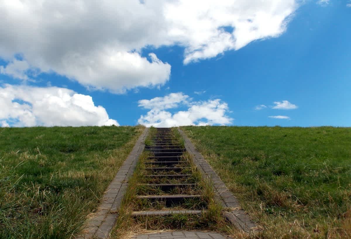 Una escalera sube una colina cubierta de hierba hacia el cielo